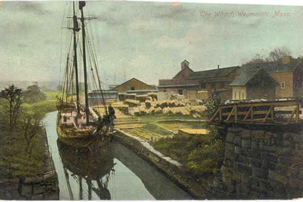 The Wharf, Weymouth, MA (old postcard), Schooner at Rhines Lumber Yard, Weymouth Landing. At Weymouth Landing a substantial number of wharfs lined the shore of the Monatiquot River, the aren now generally called the Fore River. Image provided by: Jodi Purdy-Quinlan, Vice Chairman of the Weymouth Historical Commission